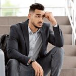 flight cancellation. upset arab man sitting with luggage at stairs in airport