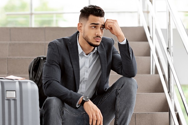 flight cancellation. upset arab man sitting with luggage at stairs in airport