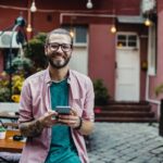 Smiling man holding phone in outdoor café.