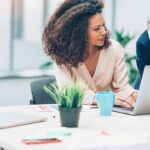 Professional women in an office setting look at a laptop screen together