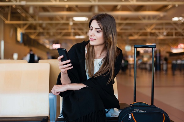 Woman at airport using smartphone with luggage