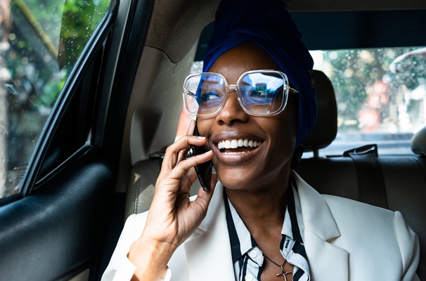 Smiling woman with glasses talking on phone in car