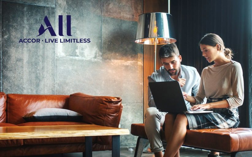 Two people looking at a laptop screen seated in a modern, elegant lobby of an ACCOR hotel.