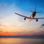Airplane flying over ocean at sunset