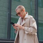 A well-dressed woman wearing tinted glasses checks a phone as she walks down the street.