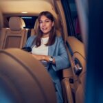 Woman holding coffee cup in car backseat.