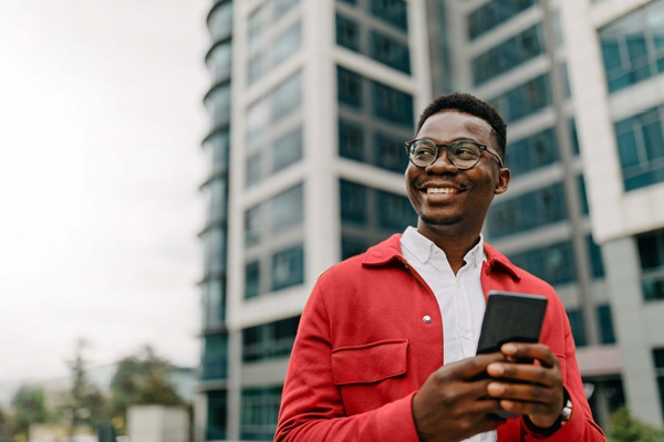 Smiling man holding smartphone outside modern building