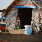 A child stands peering out of a door opening on a floating boat in a Cambodian river