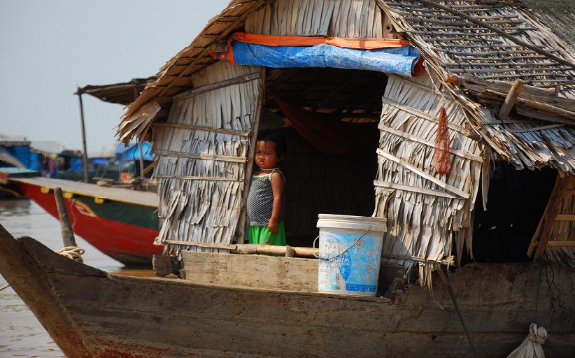 A child stands peering out of a door opening on a floating boat in a Cambodian river