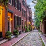 Cobblestone street with red brick buildings and lampposts.