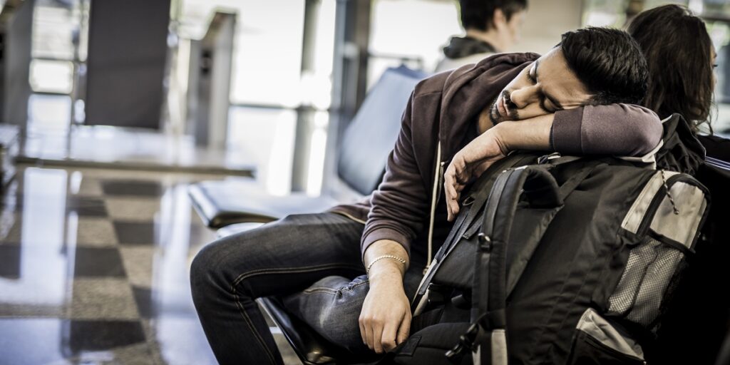 Tired traveler sleeping beside backpack in airport terminal