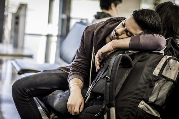 Tired traveler sleeping beside backpack in airport terminal