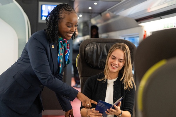 Flight attendant assists smiling passenger with passport onboard train