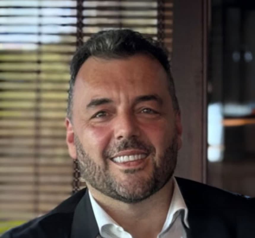 Smiling bearded man in suit before window blinds