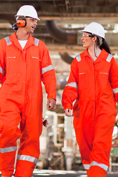 Two industrial workers in orange coveralls walking indoors