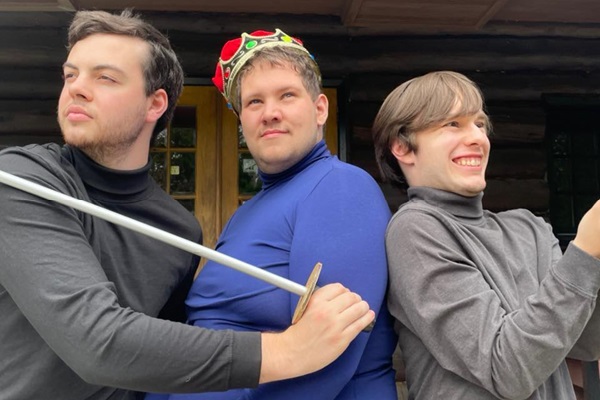 Three men pose in medieval costumes, holding swords.