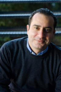 Smiling person in dark sweater sitting outdoors
