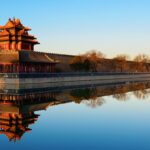 Ancient Chinese architecture reflecting in water at sunset.