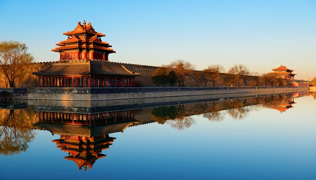 Ancient Chinese architecture reflecting in water at sunset.
