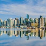 Vancouver skyline reflected in water under blue sky.