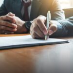 Businessperson signing a legal document at a desk.