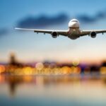Airplane flying over city lights at sunset