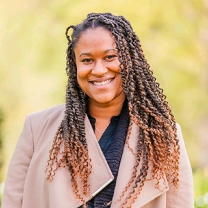 Person smiling with outdoor background, wearing coat.