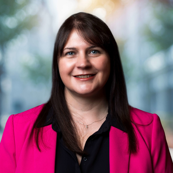 Shelley_Fletcher-Bryant 600x600 Woman smiling in pink blazer, blurred background.