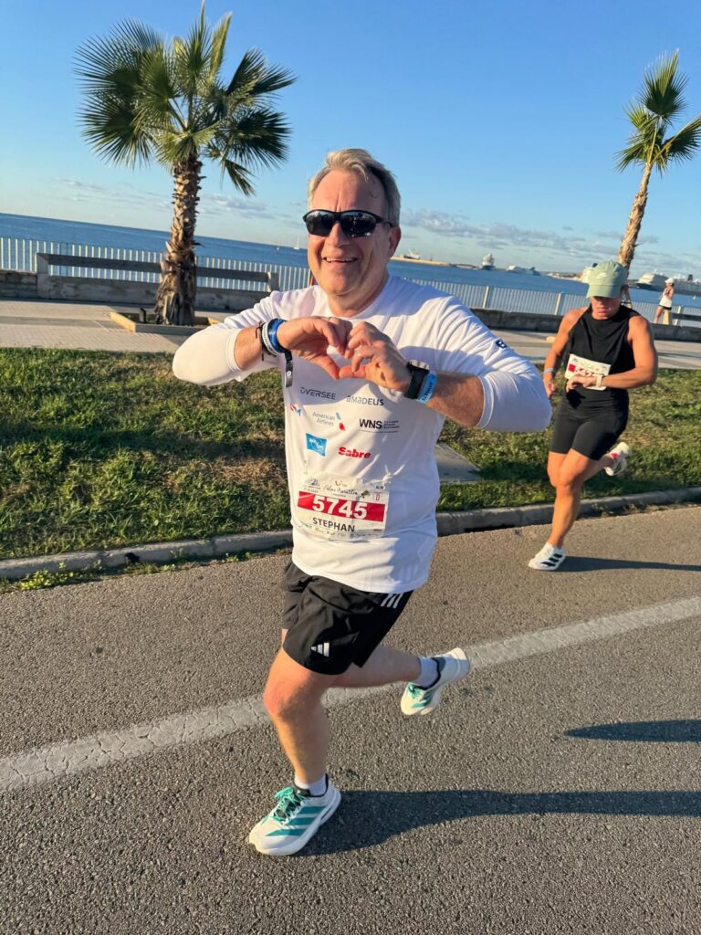 Smiling runner makes heart sign during race by ocean.
