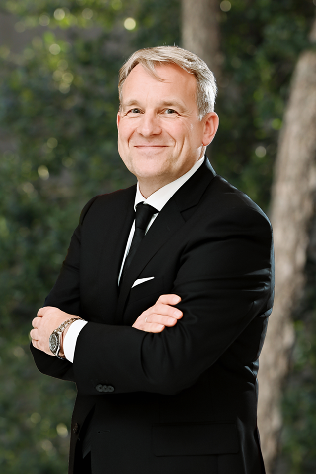 Confident man in black suit smiling outdoors.