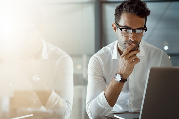 Thoughtful businessman wearing glasses works on laptop