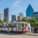 Riders on a sunny boulevard in Dallas-area wait to board a trolley car.