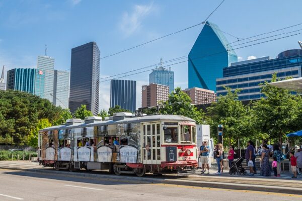 Riders on a sunny boulevard in Dallas-area wait to board a trolley car.