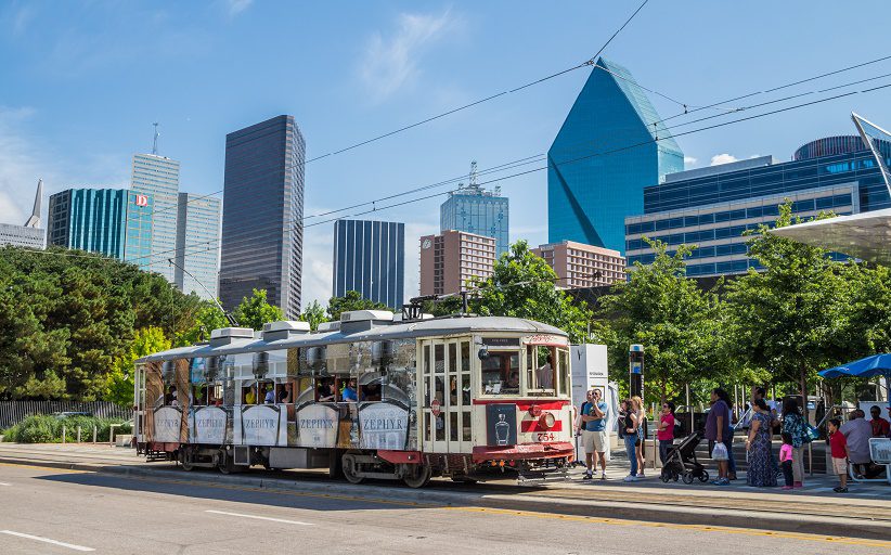 Riders on a sunny boulevard in Dallas-area wait to board a trolley car.