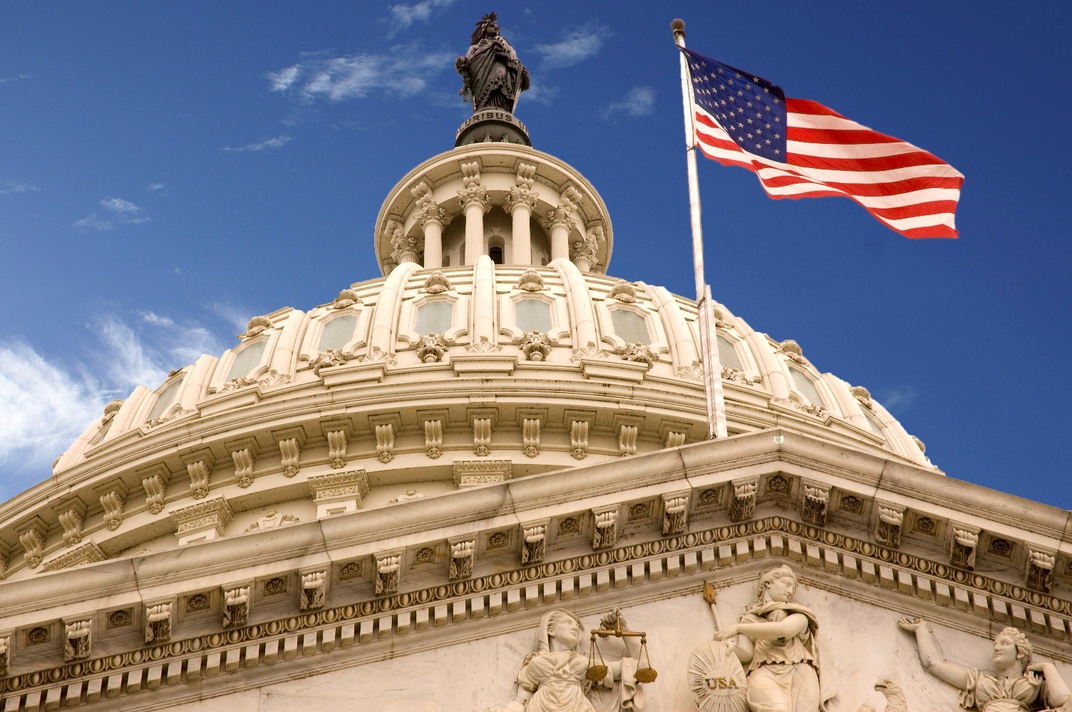 U.S. Capitol dome with American flag, blue sky.