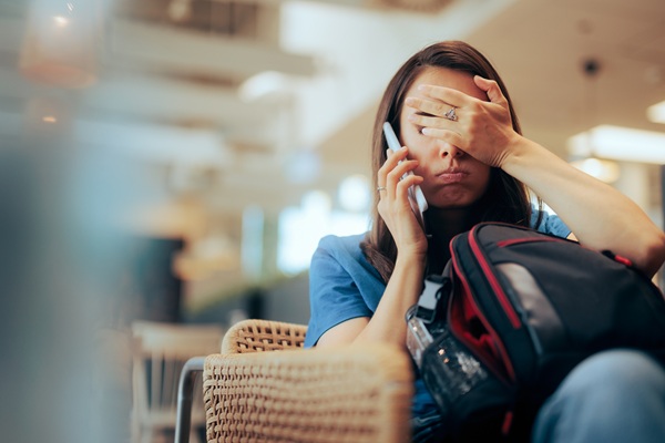 Woman on phone covers face beside luggage