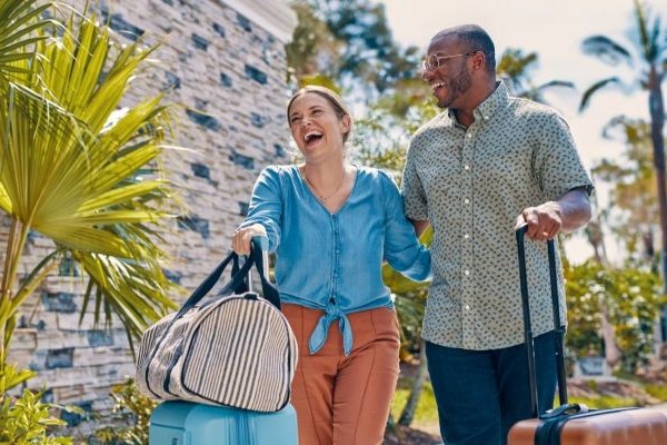 Smiling couple carrying luggage outside tropical hotel