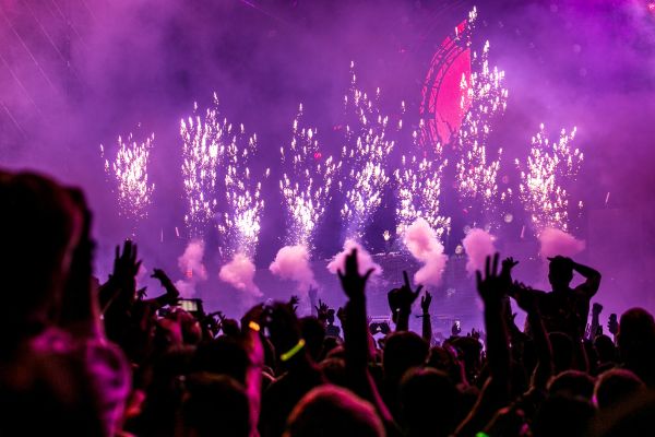Crowd cheering beneath purple fireworks at a concert
