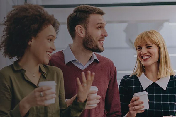 Three coworkers smiling and holding coffee cups