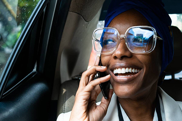 Smiling woman in glasses talks on phone inside car