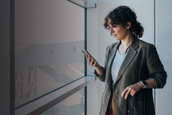 Woman in blazer checking smartphone beside large window