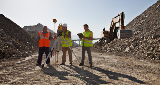 Surveyors and excavator at construction site
